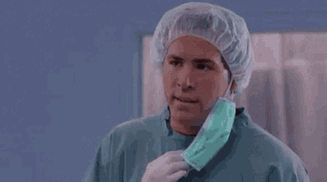 A man, actor Ryan Reynolds, in surgical scrubs and a hairnet pulls down his mask, looking puzzled: but why?
